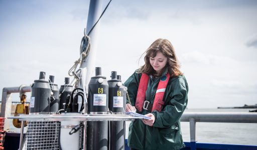 Female scientist making notes with sea water sampling experiment on research ship