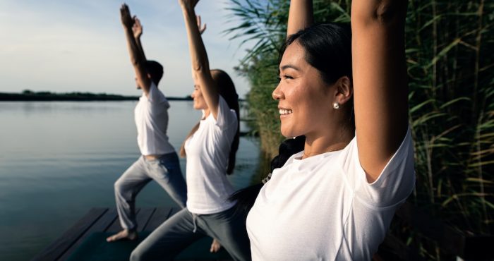 Group of people doing yoga exercises by the lake at sunset.